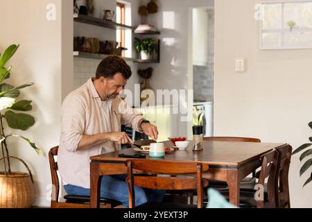 senior man enjoying breakfast at home, sitting at wooden dining table Stock Photo