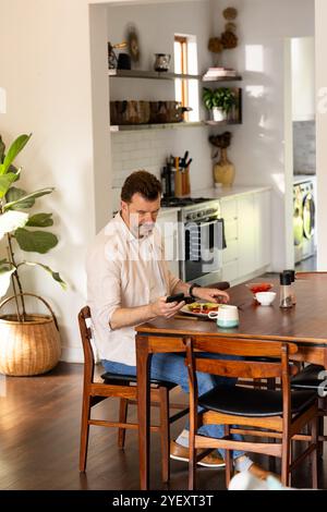 senior man using smartphone at home while enjoying breakfast at dining table Stock Photo