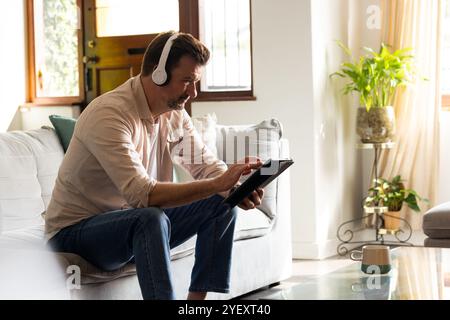senior man relaxing at home, using tablet and headphones, enjoying leisure time Stock Photo