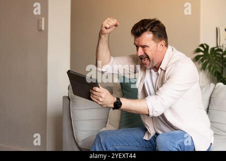 Excited senior man celebrating success while using tablet at home Stock Photo