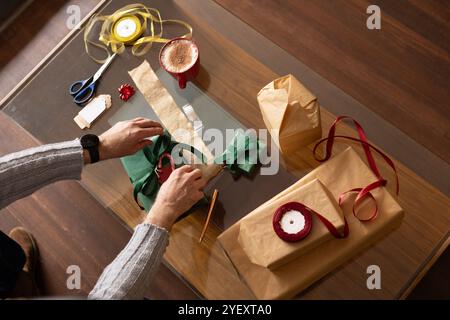 Wrapping Christmas gifts, senior man preparing presents with ribbons and hot cocoa, at home Stock Photo
