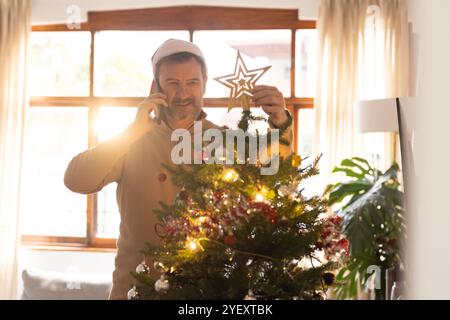 senior man decorating Christmas tree while talking on phone at home Stock Photo