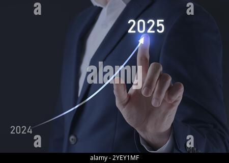 New year goals. Businessman touching line leading from 2024 to 2025 on virtual screen against black background, closeup Stock Photo