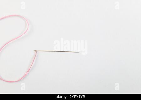 A single needle threaded with pink thread on a minimalist white background. Ready for stitching and crafting. Stock Photo
