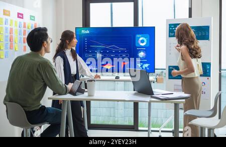 asian leader presenting a financial data and strategies in a modern office with charts and graphs displayed on a large screen Stock Photo
