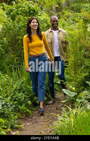 multiracial couple walking hand in hand through lush green garden ...