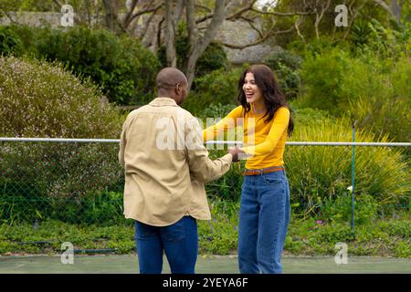 multiracial couple laughing and dancing together in lush outdoor garden Stock Photo