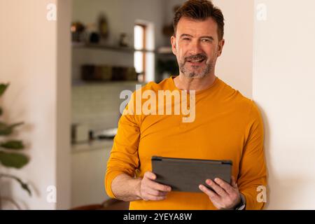 Smiling senior man holding tablet at home, enjoying relaxed holiday moment Stock Photo