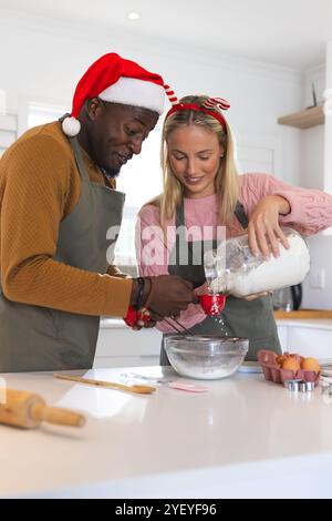 Christmas time, multiracial couple baking in kitchen wearing festive holiday hats, at home Stock Photo