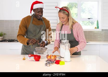 Christmas time, multiracial couple baking, wearing festive hats and aprons, at home Stock Photo