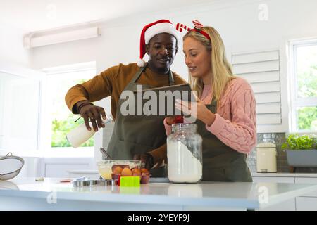 Christmas time, multiracial couple baking , using tablet for holiday recipe guidance, at home Stock Photo