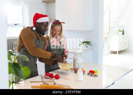 Christmas time, multiracial couple baking holiday cookies, wearing festive santa hats, at home Stock Photo