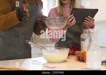 Christmas time, multiracial couple baking , using tablet for recipe guidance, at home Stock Photo