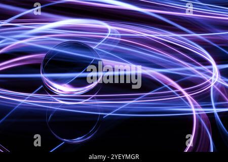 A long exposure photograph. Light painting photography. Swirls of colourful light behind and around a glass ball on a mirror. Stock Photo