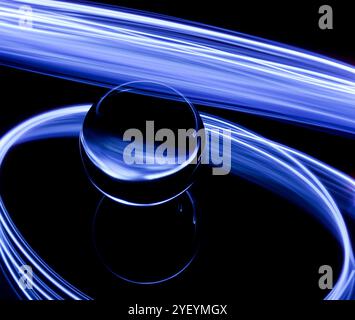 A long exposure photograph. Light painting photography. Swirls of colourful light behind and around a glass ball on a mirror. Stock Photo