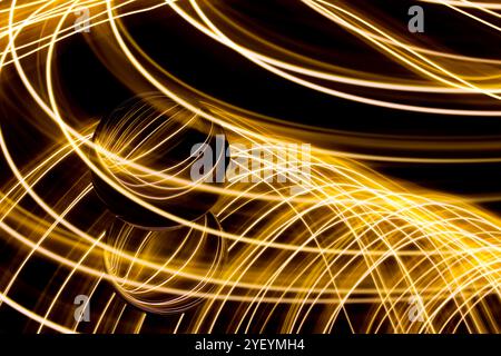 A long exposure photograph. Light painting photography. Swirls of colourful light behind and around a glass ball on a mirror. Stock Photo