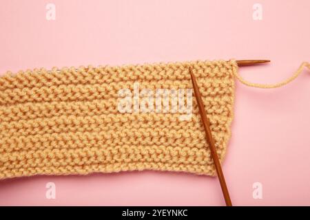 Soft beige yarns, knitting and wooden needles on pink background. Top view Stock Photo