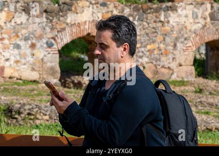YOUNG MAN SENDING A MESSAGE WITH A CELL PHONE WITH A BLACK BACKPACK Stock Photo