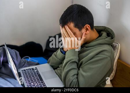 Worried teenager sitting on his bed and using a laptop in Montrouge, France. Stock Photo