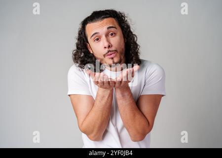 A man with curly hair blows a kiss to the camera while wearing a white t-shirt Stock Photo