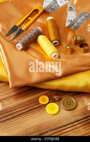 Crafting essentials arranged on golden satin fabric with sewing tools and colorful buttons scattered around Stock Photo