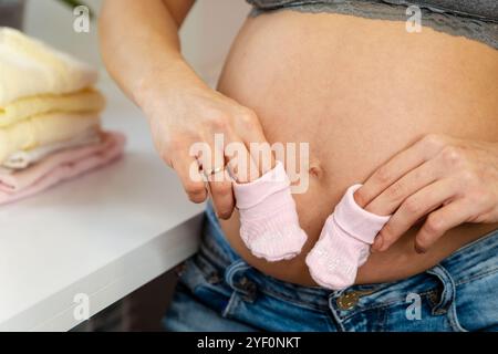 Close up pregnant womans hand holding knitting sock placing on her belly. Stock Photo
