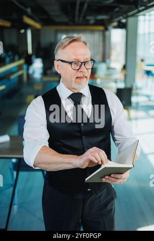 Male financier with gray hair reviewing financial reports and contracts, adult boss working with papers at office workplace. Stock Photo