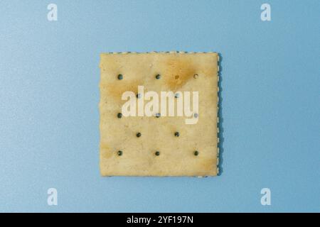 A single square saltine cracker, with a textured surface and small holes, on a blue background. Stock Photo