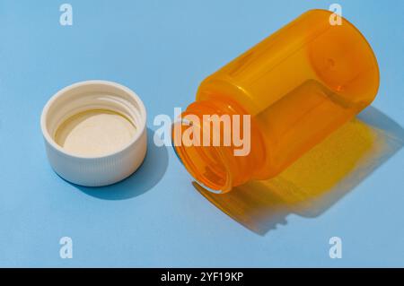 An empty orange plastic pill bottle lies on its side on a blue surface. Need medication prescription refill Stock Photo