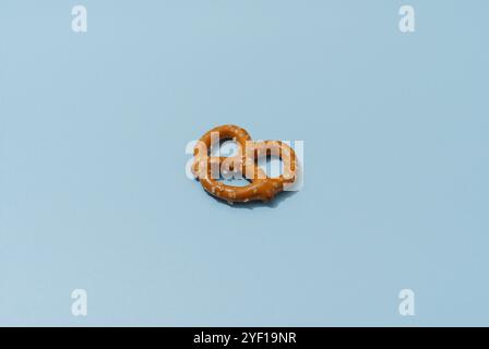 A single, brown pretzel with salt crystals sits on a blue background. The pretzel is in focus, while the background is slightly blurred. The lighting Stock Photo