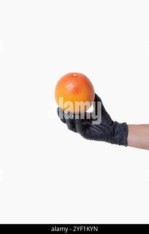 Hand with a black glove holds a grapefruit on bright background. Creative concept of clean healthy food Stock Photo