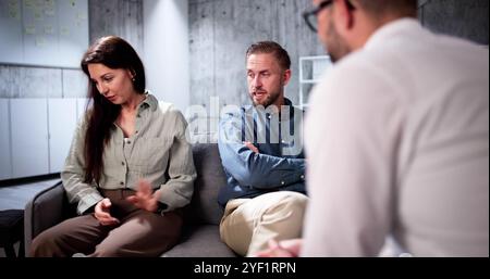 Happy Young Couple Sitting On Sofa Consulting With Psychologist Stock Photo