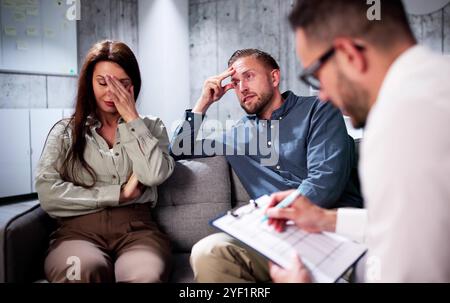 Sad Young Couple Sitting On Sofa With Female Psychologist Stock Photo