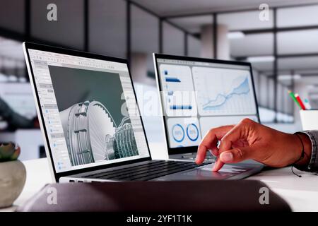 African American Male Engineer Developing Mechanical Parts Using 3D CAD Software On Laptop At Factory Office Stock Photo