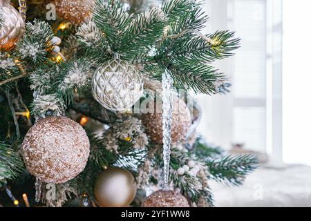 Christmas tree branch with frost decorated with shimmering ornaments and sparkling lights on cozy room background. Festive decorations for winter holi Stock Photo