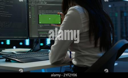 Zoom in on green screen mobile phone used by data center employee troubleshooting issues. Engineer uses mockup smartphone device in server hub, establishing performance benchmarks, camera A Stock Photo