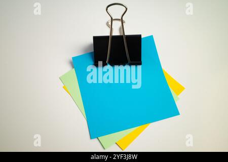 Binder clip holding multiple colorful sheets of paper stacked together Stock Photo