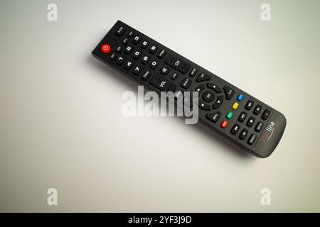 Black TV remote control with colorful buttons placed on a white surface Stock Photo
