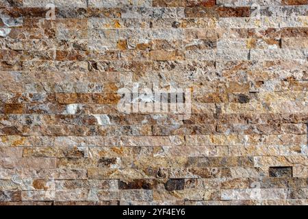 Wall made of stacked stone tiles in various shades of brown, beige, gray, and white. The stones are arranged horizontally with a rough texture, giving Stock Photo