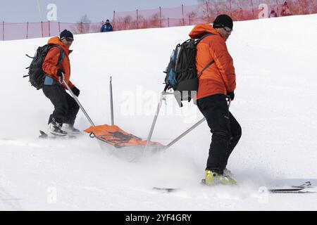 KAMCHATKA, RUSSIA, MARCH 28, 2019: Rescuers Kamchatka Rescue Squad on alpine ski with stretcher skiing down mount slope for first medical aid, evacuat Stock Photo