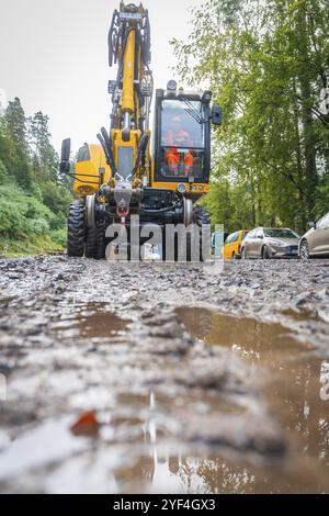 A yellow excavator works on a muddy road in the forest with two construction workers in sight, track construction, Hermann Hessebahn, Calw, Black Fore Stock Photo