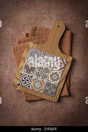 Wooden cutting board with ceramic tiles, on a kitchen towel, top view, food background Stock Photo