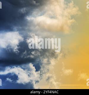 Amazing view of dramatic blue thunderclouds and stunning yellow-golden fluffy clouds illuminated by rays of sun. Natural meteorology background, cloud Stock Photo