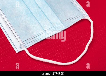 Fragment of blue medical face mask on bright red background of non-woven fabric. Close-up view of medicine concept coronavirus pandemic covid-19 disea Stock Photo