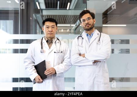Doctors confidently standing in hospital hallway, wearing white coats and stethoscopes. Represents professionalism, teamwork in healthcare. Perfect for concepts of medical care, expertise. Stock Photo