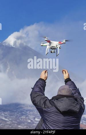Male launches flying drone quadcopter UAV with digital camera on background of volcano eruption, mount peak erupting ashes, volcanic gas from active c Stock Photo