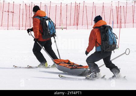 KAMCHATKA, RUSSIA, MARCH 28, 2019: Rescuers Kamchatka Rescue Squad on alpine ski with stretcher skiing down mount slope for first medical aid, evacuat Stock Photo