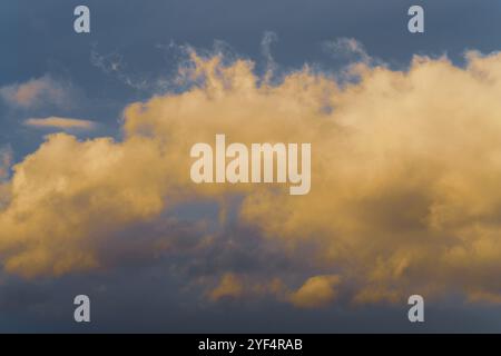 Beautiful golden fluffy clouds illuminated by disappearing rays at sunset, thunderclouds floating across sunny blue sky to change season weather. Natu Stock Photo