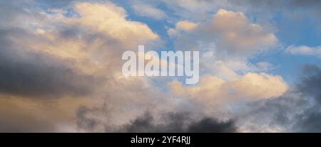 Beautiful colorful panorama of summer golden fluffy clouds illuminated disappearing rays at sunset and dramatic dark thunderclouds in sunny blue sky. Stock Photo