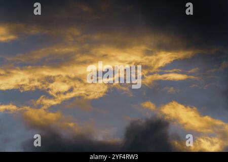 Stunning fluffy thunderstorm clouds illuminated by disappearing rays at sunset and dark thunderclouds floating across sunny blue sky to change season Stock Photo
